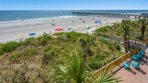 A beach with a pier, beach umbrellas, and a wooden deck with chairs. - Rest, pure & simple! Gorgeous ocean view, large balcony w/pool & hot tub in popular Cherry Grove (North Myrtle Beach)