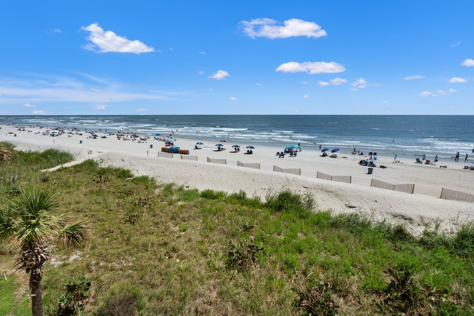 A beach with a sandy shore, a wooden fence, and a clear sky.