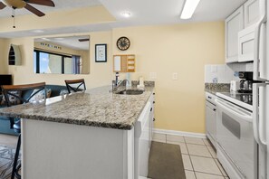 A kitchen with a granite countertop, white cabinets, a built-in oven, and a clock on the wall.