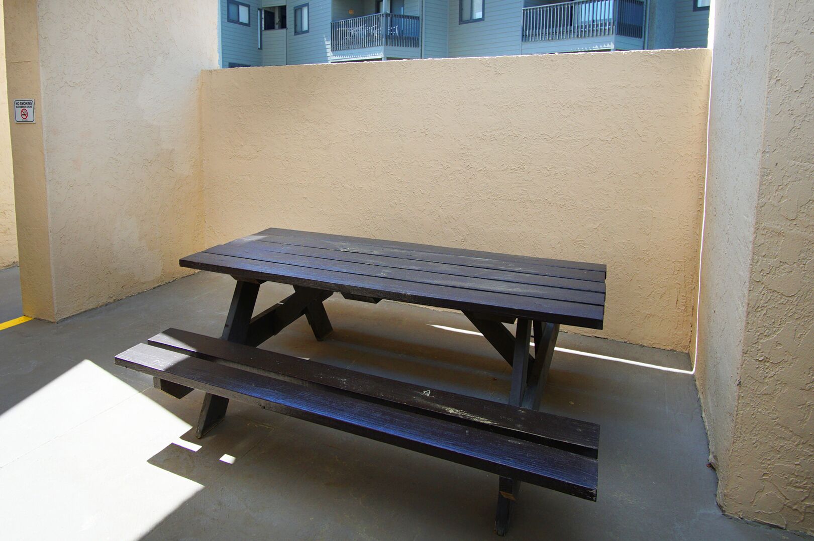 A picnic table with benches in an outdoor area with a plain wall and a building in the background.