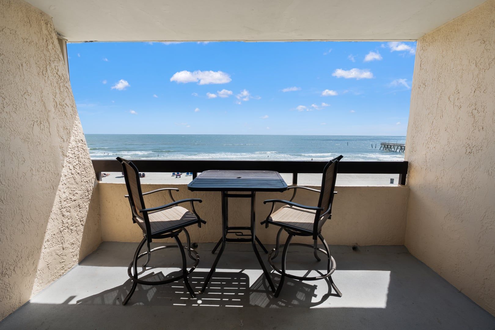 Ein Balkon mit Tisch und zwei Stühlen, mit Blick auf Strand und Meer.