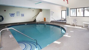 An indoor swimming pool with clear pool rules signs, a lifeguard chair, and a view of the outside through a window.