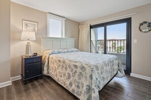 A bedroom with a bed, nightstand, lamp, and a view of the outside balcony.