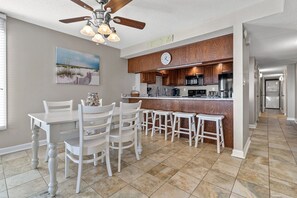 A modern kitchen with a central island, white bar stools, and a ceiling fan.