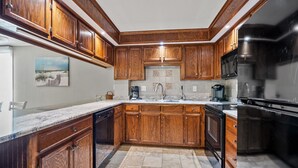 A kitchen with wooden cabinets, a black refrigerator, and a marble countertop. - This view! You'll love this roomy oceanfront condo rental w/pool, sundeck in popular North Myrtle (North Myrtle Beach)