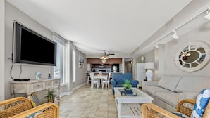 A spacious living room with a television, wicker chairs, a sofa, and a dining area with a table and chairs. - This view! You'll love this roomy oceanfront condo rental w/pool, sundeck in popular North Myrtle (North Myrtle Beach)