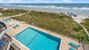 A pool area with lounge chairs and a view of the beach and ocean. - This view! You'll love this roomy oceanfront condo rental w/pool, sundeck in popular North Myrtle (North Myrtle Beach)