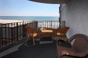 Een balkon met rieten meubilair met uitzicht op een strand.