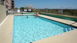 Una piscina rectangular con agua azul cristalina, rodeada por una plataforma de hormigón y una valla metálica.