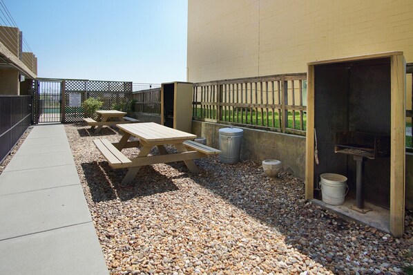 Een terras buiten met picknicktafels, een barbecue en een grindpad.