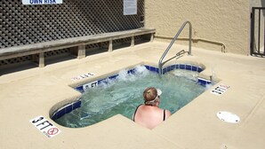 Un jacuzzi con una persona adentro, rodeado de señales de seguridad y un banco de madera.