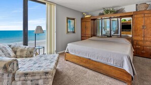 Un dormitorio con una cama grande, un armario de madera, una silla y vistas a la playa.