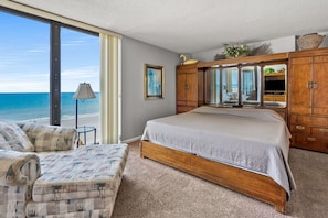 A bedroom with a large bed, a wooden wardrobe, a chair, and a view of the beach. - Updated & spacious oceanfront family condo rental w/amazing views, pool, hot tubs in North Myrtle! (North Myrtle Beach)