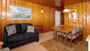 Een gezellige kamer met een houten lambrisering, een lijst met foto, een bank met decoratieve kussens en een eettafel met stoelen.