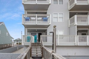 A multi-story residential building with a central staircase, balconies with railings, and a door with a blue awning.