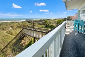 A balcony with a view of the beach, a wooden staircase, and a white railing.