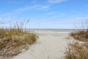 A sandy beach path leading to the ocean, surrounded by grass.