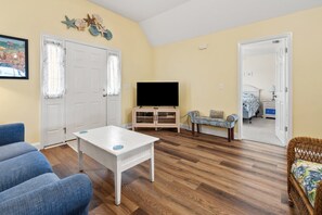 Sala de estar com mesa de centro branca, sofá azul e televisão sobre um móvel de madeira.