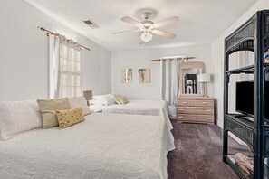 Une chambre d’hôtel avec deux lits, un ventilateur de plafond, une commode et un téléviseur posé sur un meuble.