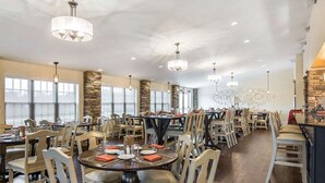 Un vaste espace dédié à la salle à manger, avec de nombreuses tables et chaises, de grandes fenêtres et un mur décoratif en pierre.