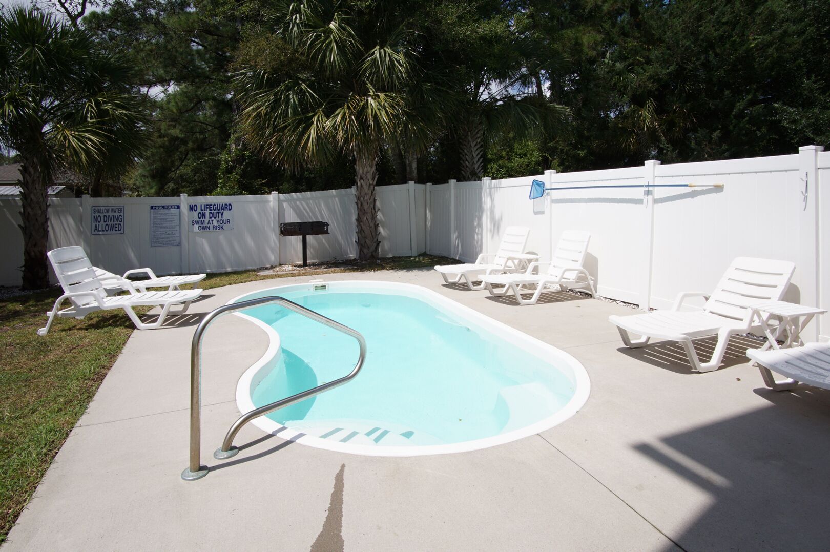 Una piscina con una escalera metálica, rodeada de sillas de descanso blancas y palmeras.