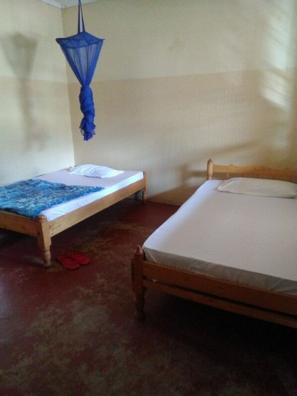 Ein Zimmer mit zwei Holzbetten, eines mit blauer Bettdecke und das andere mit weißer Bettdecke. Ein blaues Moskitonetz hängt von der Decke.