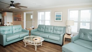 Un salon avec un ensemble de canapés en cuir turquoise, une table basse en verre et un ventilateur de plafond.