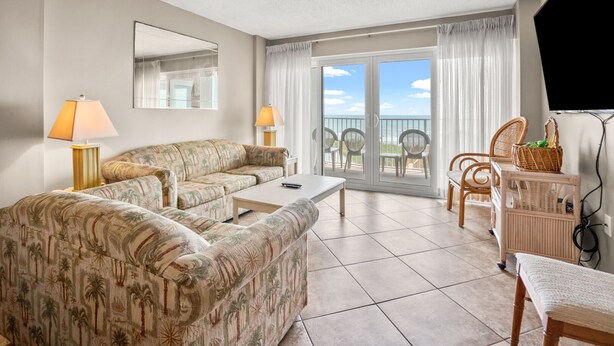 A living room with a sofa, a coffee table, and a TV stand. There is a balcony with a view of the sky and a chair. - Oceanfront panoramic views, indoor pool, Jacuzzi, balcony--in favorite North Myrtle Beach (North Myrtle Beach)