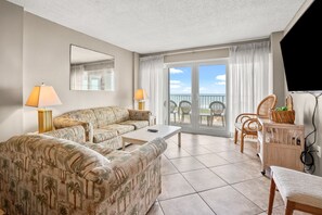 A living room with a sofa, a coffee table, and a TV stand. There is a balcony with a view of the sky and a chair. - Oceanfront panoramic views, indoor pool, Jacuzzi, balcony--in favorite North Myrtle Beach (North Myrtle Beach)