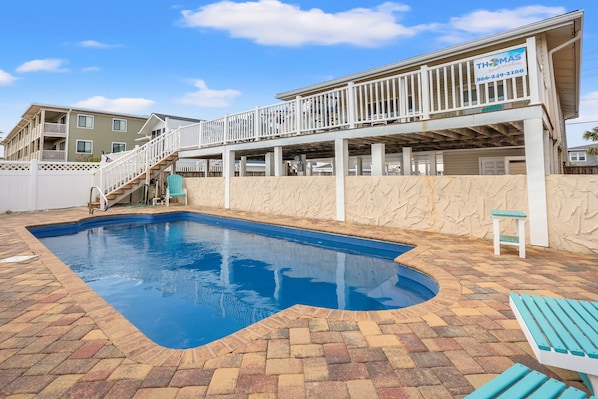 Une piscine bordée de pierres, une terrasse en bois et une clôture blanche.
