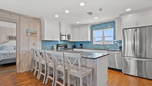 Una cocina moderna con armarios blancos, un refrigerador de acero inoxidable, un microondas y una isla grande con taburetes de bar.