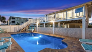Una piscina de borde curvo, rodeada por un patio de ladrillo y sillas azules.