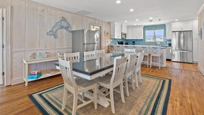 Una cocina moderna con armarios blancos, electrodomésticos de acero inoxidable y una zona de comedor con mesa de vidrio y sillas blancas.