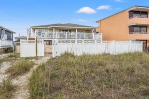 Une propriété située en bord de mer, dotée d’une entrée sécurisée par un portail, d’un patio couvert et d’un bâtiment à deux étages avec un balcon.