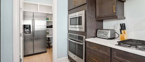 A kitchen with a refrigerator, microwave, toaster, and oven.