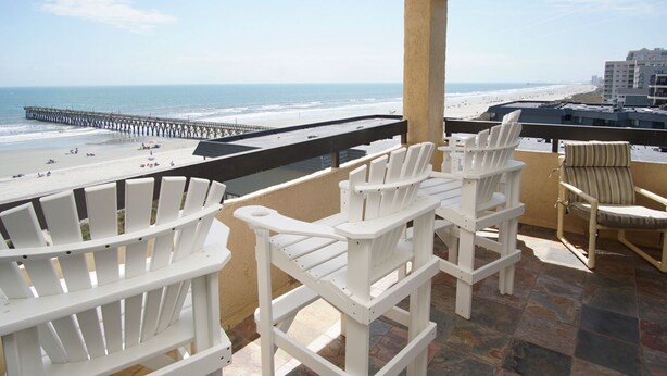 A balcony with white Adirondack chairs overlooking a beach and pier. - Charming & comfortable condo with ocean view, balcony, w/pool & hot tub in popular Cherry Grove (North Myrtle Beach)