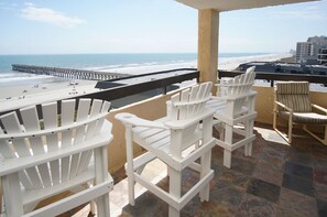 A balcony with white Adirondack chairs overlooking a beach and pier. - Charming & comfortable condo with ocean view, balcony, w/pool & hot tub in popular Cherry Grove (North Myrtle Beach)