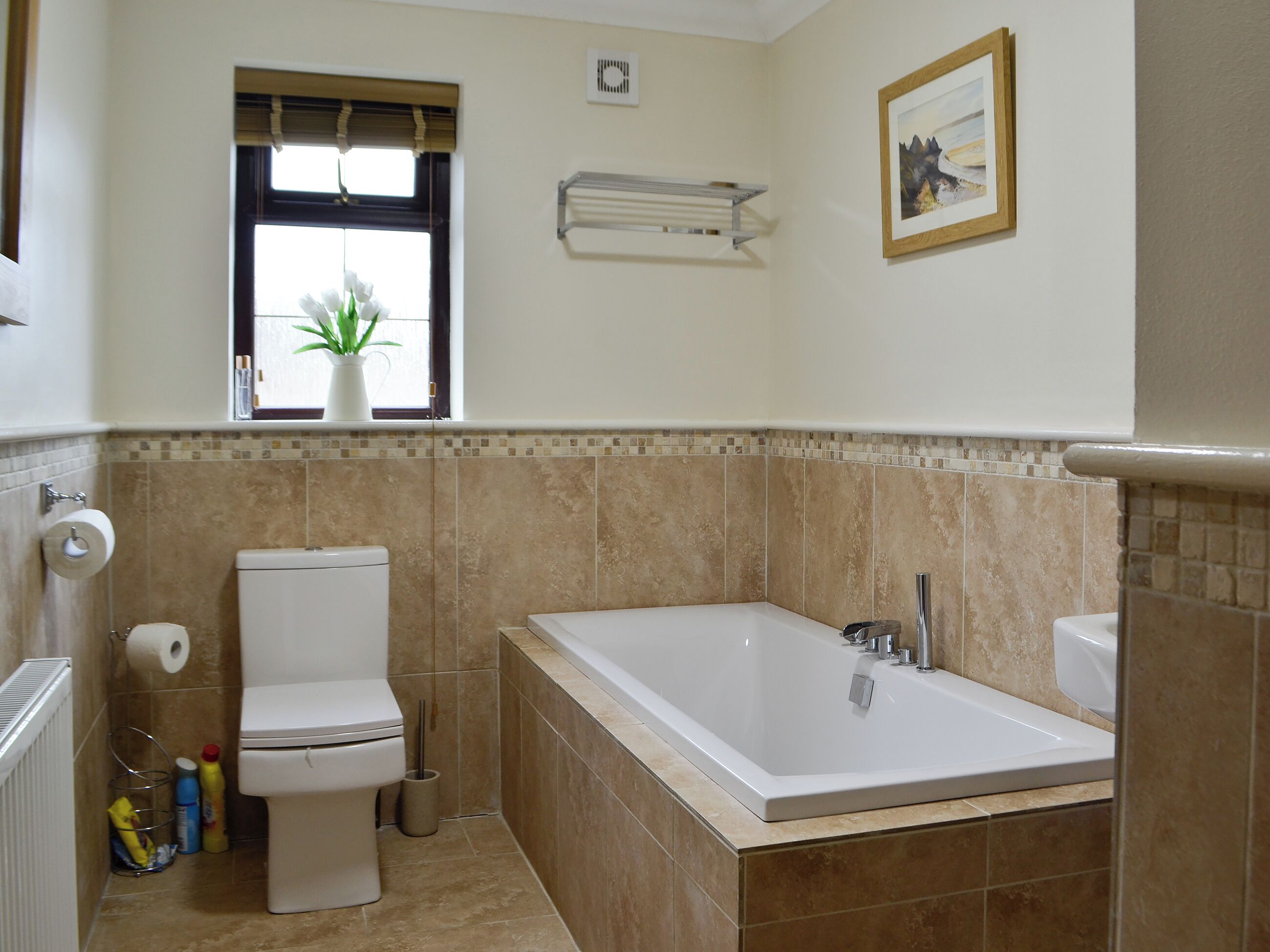 A bathroom with a toilet, a bathtub, a window with a plant, and a picture on the wall.