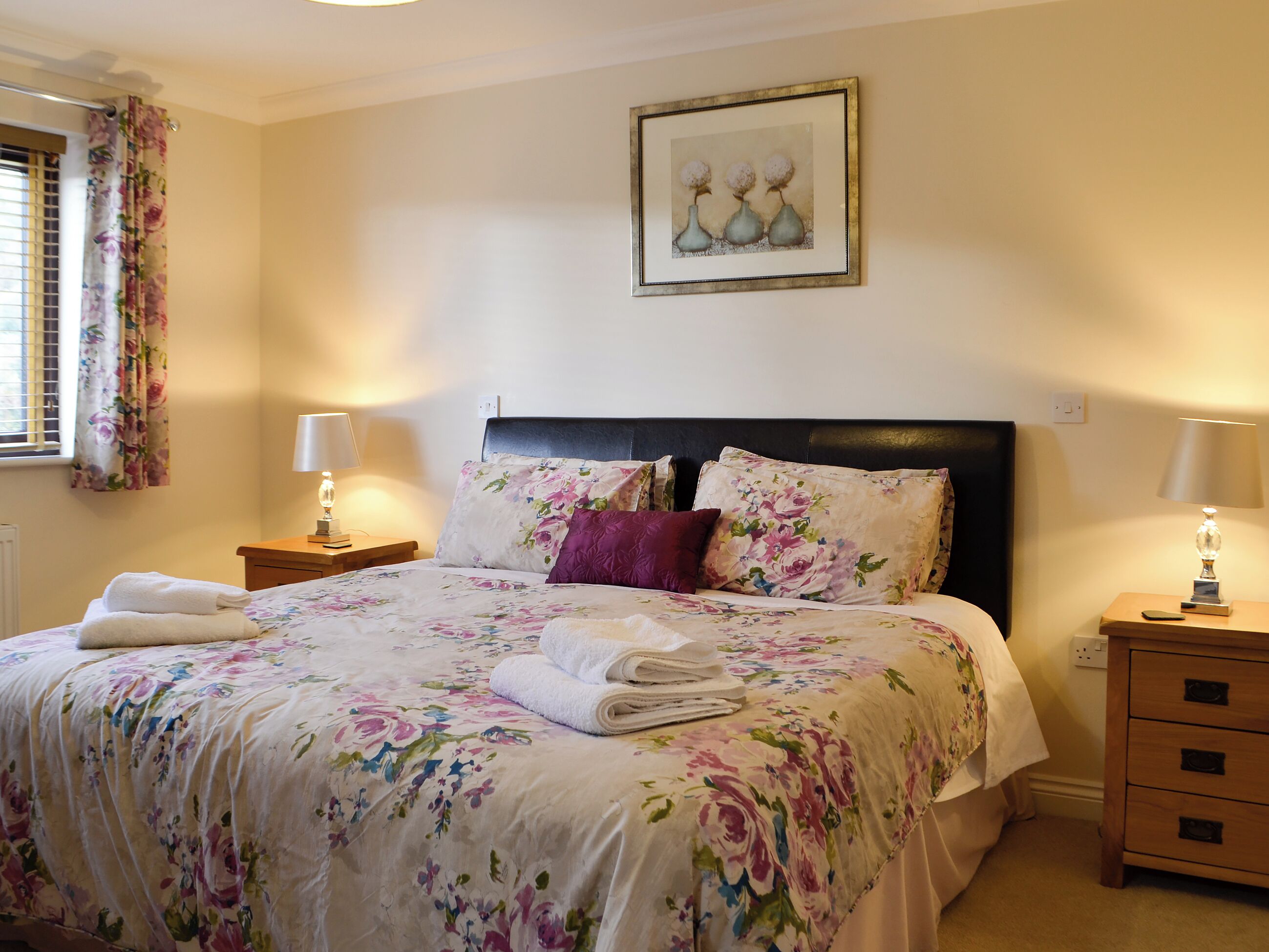 Ein ordentlich gemachtes Bett mit Blumenmuster auf der Bettwäsche, einem Kopfteil und zwei Nachttischlampen.
