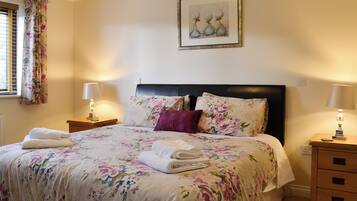 Ein ordentlich gemachtes Bett mit Blumenmuster auf der Bettwäsche, einem Kopfteil und zwei Nachttischlampen.