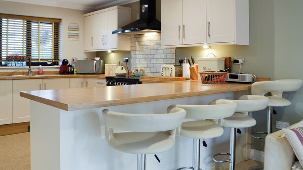 A modern kitchen with a central island, bar stools, and a window with blinds. - 4 bedroom accommodation in Lower Cwm-twrch, near Ystradgynlais (Lower Cwm-twrch, near Ystradgynlais)