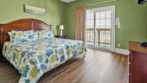 Un dormitorio con cama de madera, una mesita de noche, lámpara, ventana con vistas y ventilador de techo.