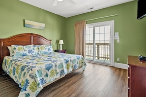A bedroom with a wooden bed, a nightstand, a lamp, a window with a view, and a ceiling fan.