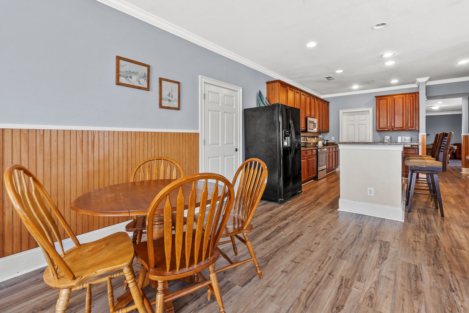 A spacious kitchen with wooden cabinets, a black refrigerator, and a dining area with wooden chairs and a table.