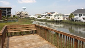 Eine Holzterrasse mit einer Bank bietet Blick auf ruhiges Wasser, umgeben von Wohngebäuden mit Balkonen und einem Wasserturm im Hintergrund.