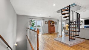 A spacious living area with a wooden staircase leading to a mezzanine, a built-in bookshelf, and a view through a glass door. - Gorgeous blvd home, pet-friendly w/private pool, and beautiful decks in North Myrtle (North Myrtle Beach)