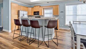Une cuisine moderne avec des meubles en bois, un îlot central doté de tabourets, et un coin repas avec une table et des chaises.