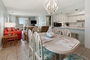 A modern kitchen with white cabinets, a dining table with floral placemats, and a red sofa in the living area.