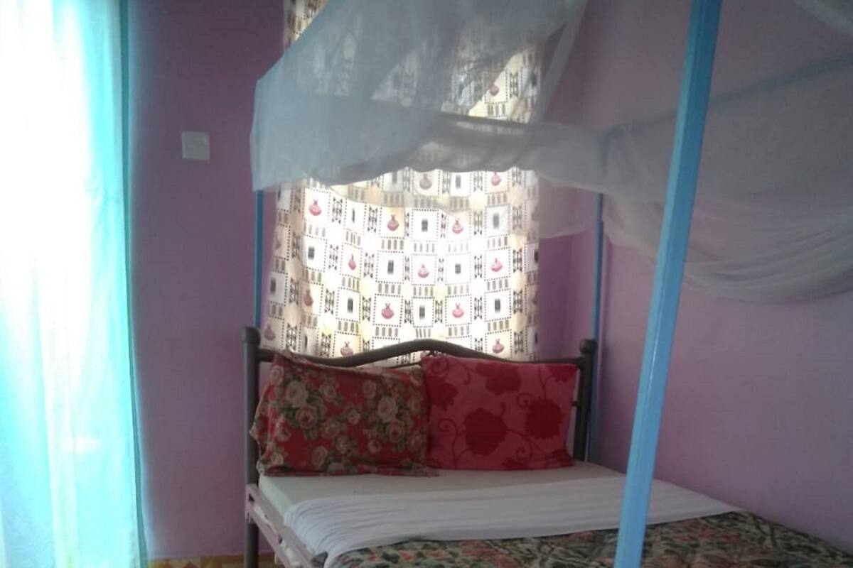 Uma cama de solteiro com dossel, parede estampada e chão de azulejos.