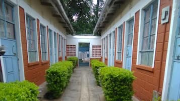 Two-story buildings with windows flank a paved corridor lined with greenery.